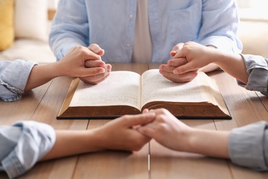 Photo of Family with Bible praying at wooden table indoors, closeup