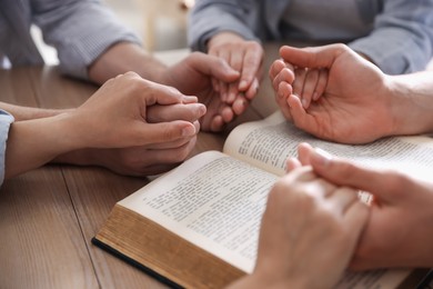Photo of Family with Bible praying at wooden table indoors, closeup