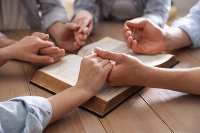 Photo of Family with Bible praying at wooden table indoors, closeup