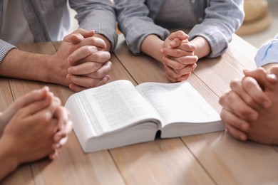 Photo of Family with Bible praying at wooden table indoors, closeup