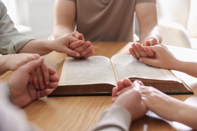 Photo of Family with Bible praying at wooden table indoors, closeup