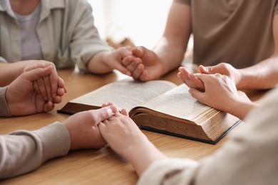 Photo of Family with Bible praying at wooden table indoors, closeup
