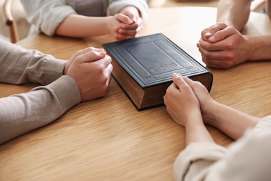 Photo of Family with Bible praying at wooden table indoors, closeup