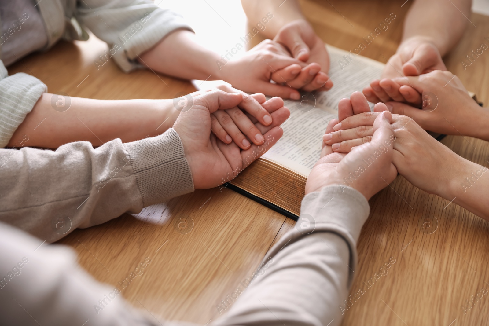Family with Bible praying at wooden table indoors, closeup Photo of Family with Bible praying at wooden table indoors, closeup