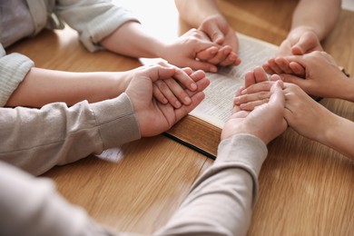 Photo of Family with Bible praying at wooden table indoors, closeup