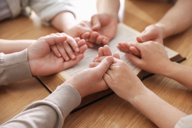 Photo of Family with Bible praying at wooden table indoors, closeup