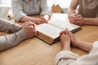Photo of Family with Bible praying at wooden table indoors, closeup