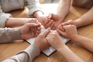 Photo of Family with Bible praying at wooden table indoors, closeup
