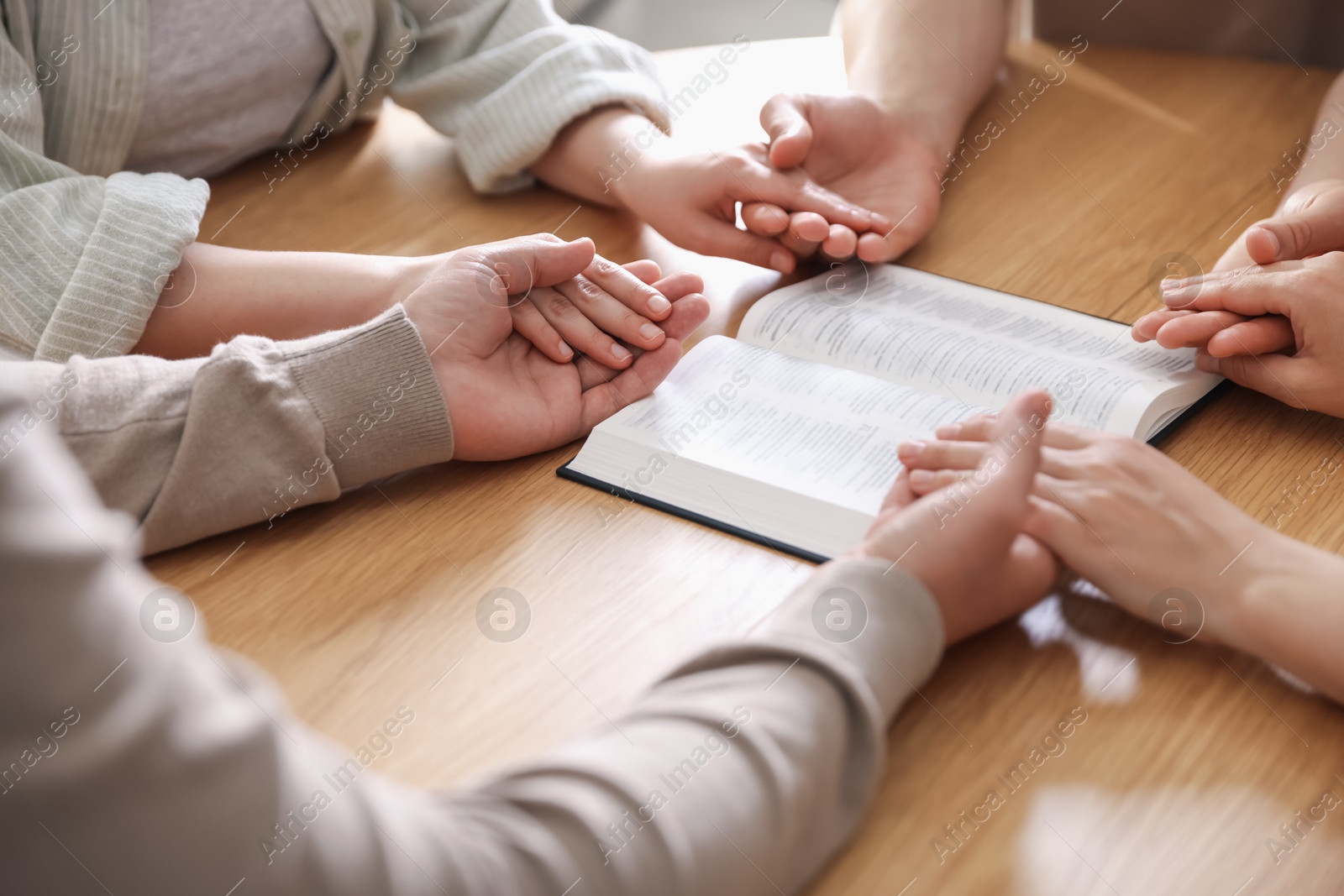Family with Bible praying at wooden table indoors, closeup Photo of Family with Bible praying at wooden table indoors, closeup