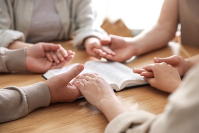 Photo of Family with Bible praying at wooden table indoors, closeup