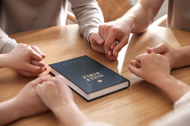 Photo of Family with Bible praying at wooden table indoors, closeup