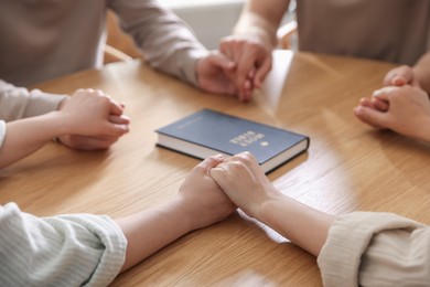 Photo of Family with Bible praying at wooden table indoors, closeup