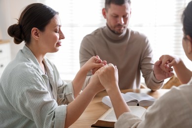 Photo of Family with Bibles praying at wooden table indoors