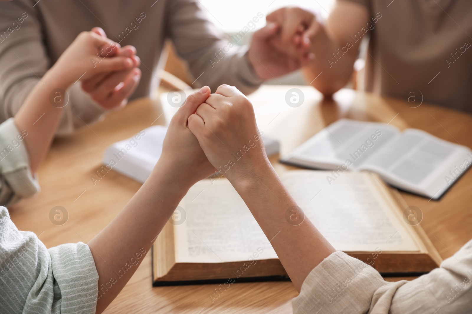 Family with Bibles praying at wooden table indoors, closeup Photo of Family with Bibles praying at wooden table indoors, closeup