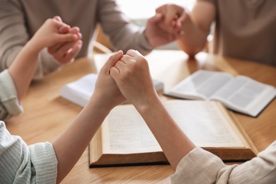 Photo of Family with Bibles praying at wooden table indoors, closeup