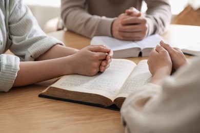 Photo of Family with Bibles praying at wooden table indoors, closeup