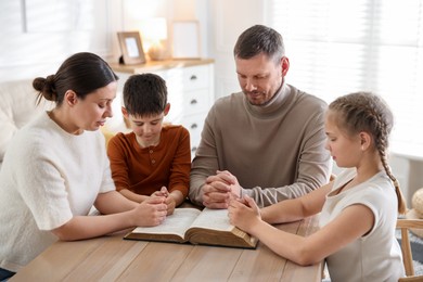 Photo of Family with Bible praying at table indoors