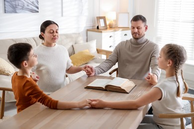 Photo of Family with Bible praying at table indoors