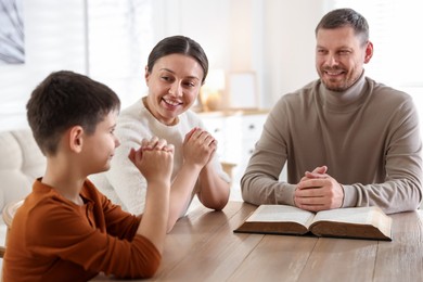 Photo of Family with Bible praying at table indoors