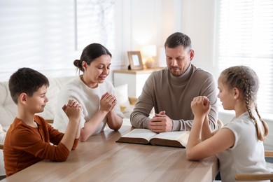 Photo of Family with Bible praying at table indoors