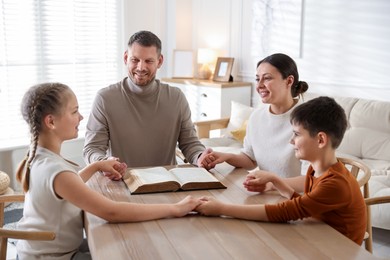 Photo of Family with Bible praying at table indoors
