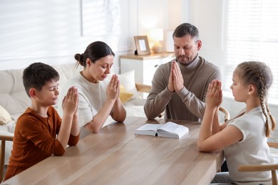 Photo of Family with Bible praying at table indoors