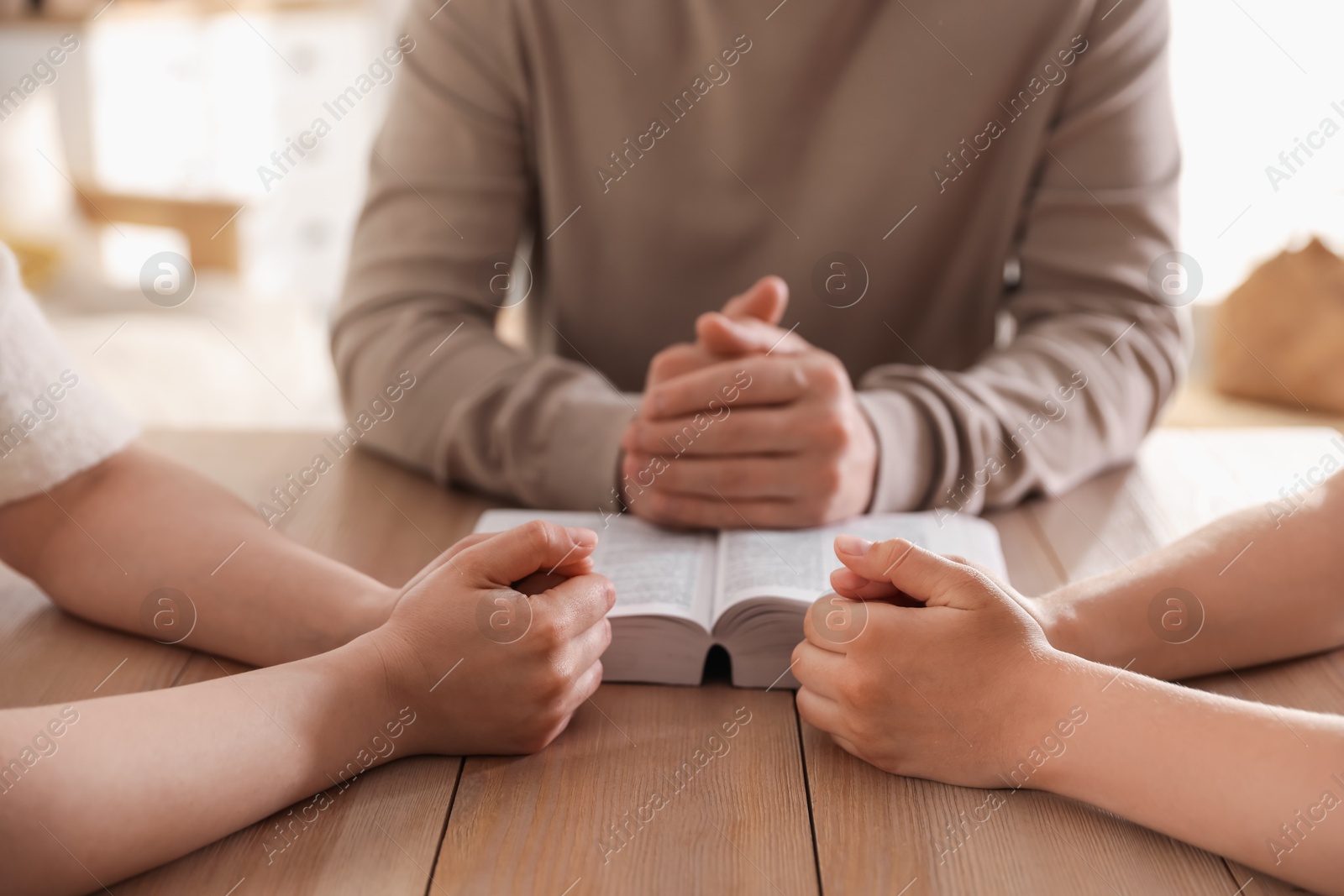 Family with Bible praying at table indoors, closeup Photo of Family with Bible praying at table indoors, closeup