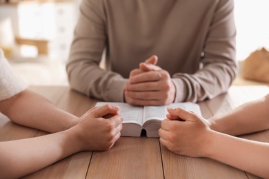 Photo of Family with Bible praying at table indoors, closeup