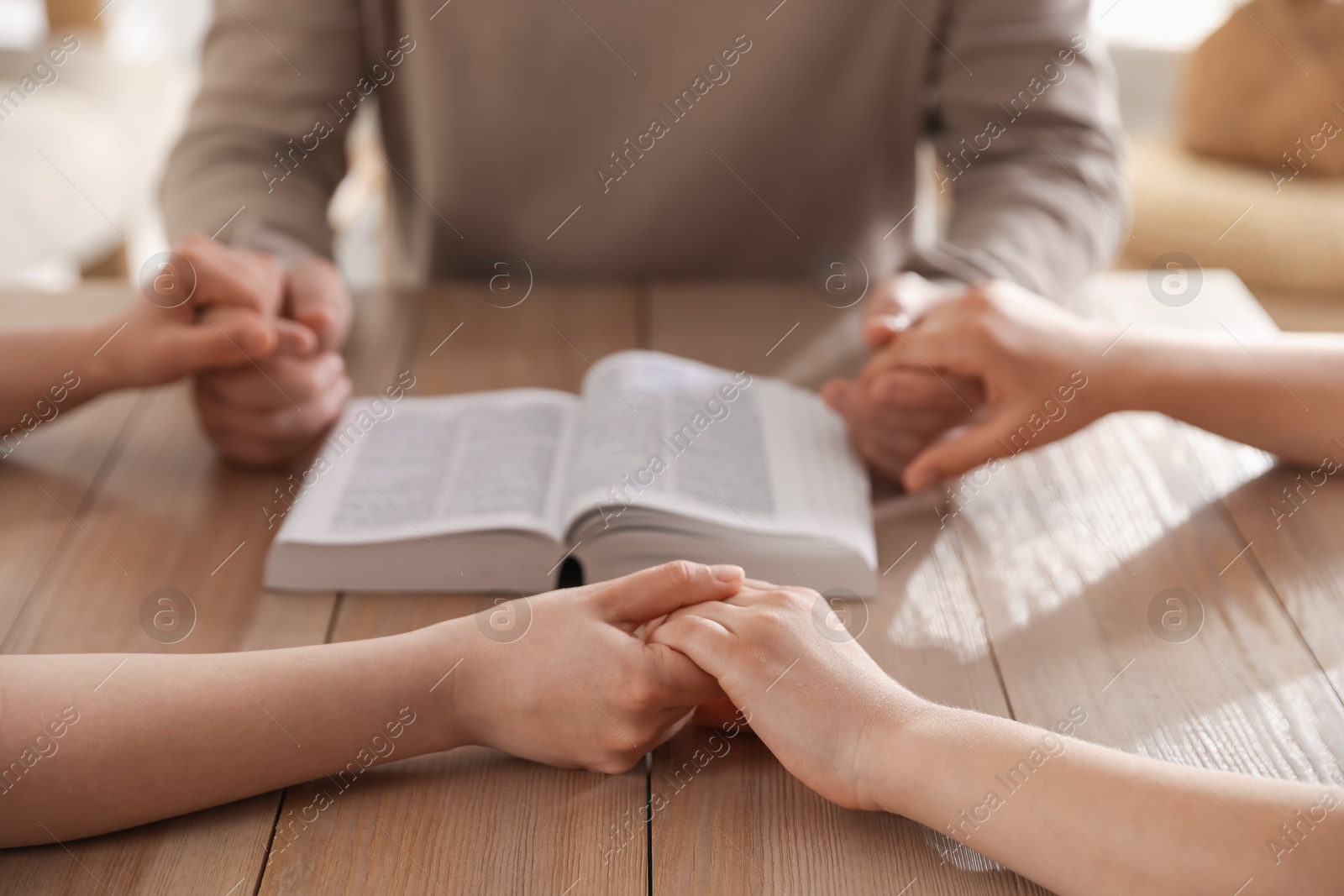 Family with Bible praying at table indoors, closeup Photo of Family with Bible praying at table indoors, closeup