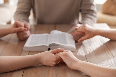 Photo of Family with Bible praying at table indoors, closeup