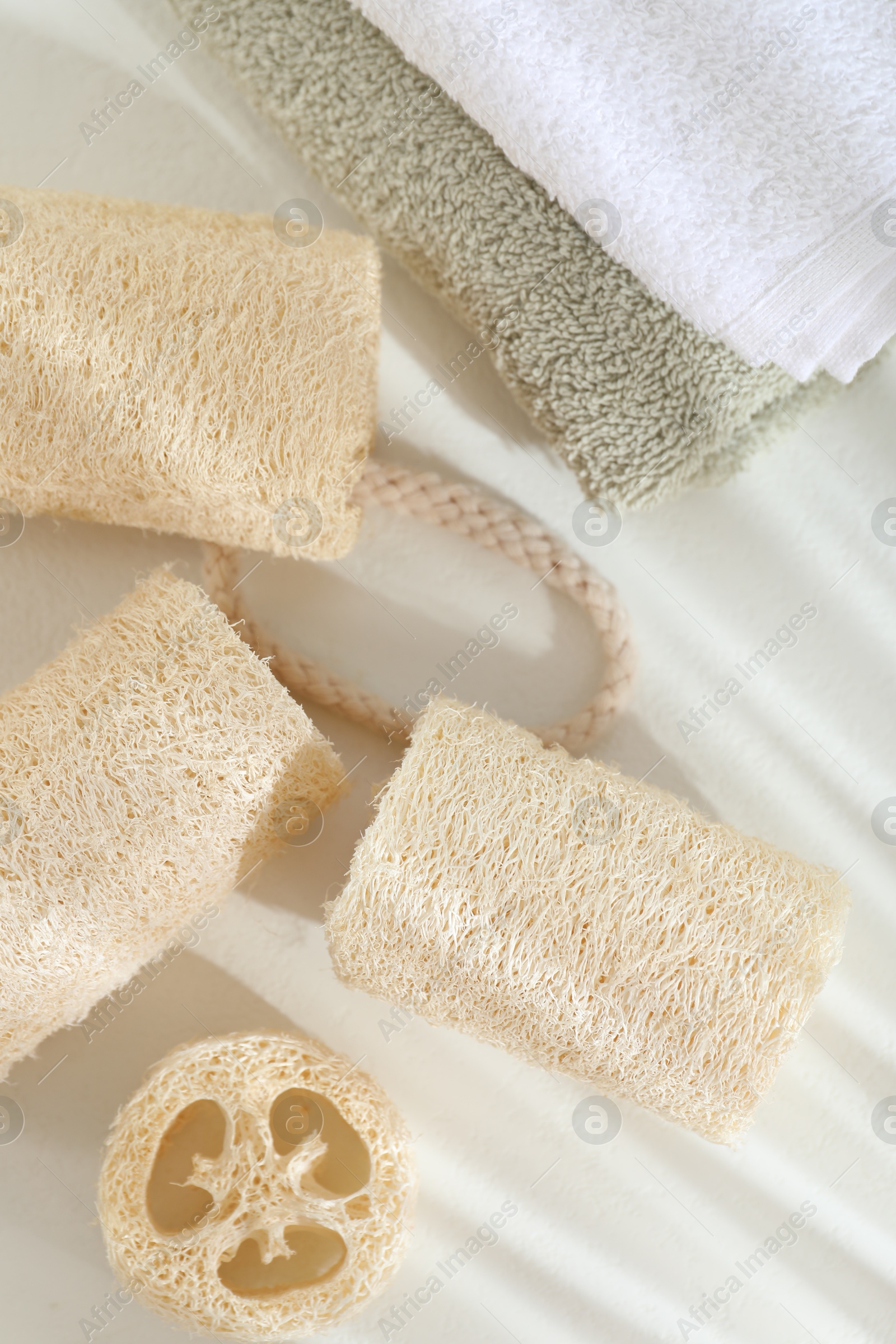 Different loofah sponges and towels on white table, flat lay Photo of Different loofah sponges and towels on white table, flat lay