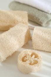 Photo of Different loofah sponges and towels on white table, closeup