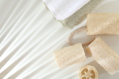 Photo of Different loofah sponges and towels on white table, flat lay. Space for text