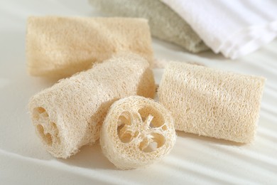 Photo of Different loofah sponges and towels on white table, closeup