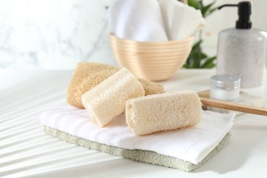 Photo of Different loofah sponges and towels on white table, closeup