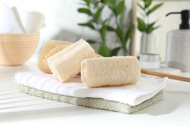 Photo of Different loofah sponges and towels on white table, closeup