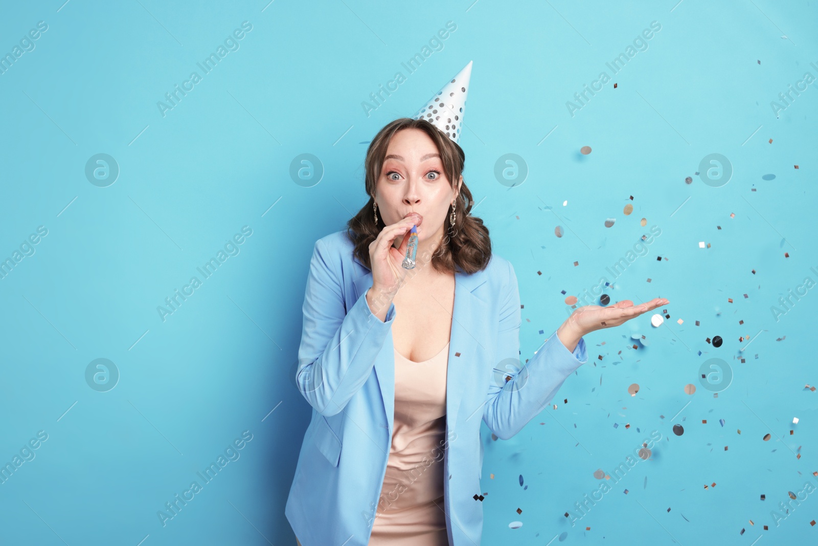 Birthday celebration. Woman with party horn and confetti on light blue background Photo of Birthday celebration. Woman with party horn and confetti on light blue background