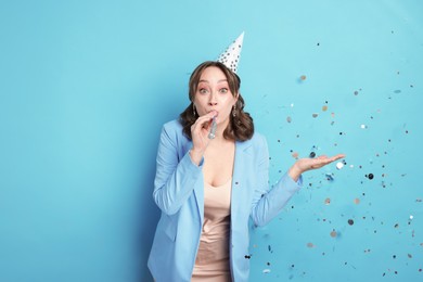 Photo of Birthday celebration. Woman with party horn and confetti on light blue background