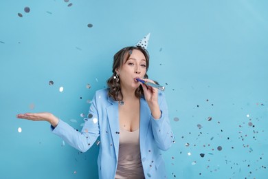Photo of Birthday celebration. Woman with party horn and confetti on light blue background