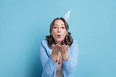 Photo of Birthday celebration. Woman blowing air kiss on light blue background