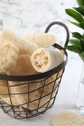 Photo of Different loofah sponges in basket on light grey table, closeup