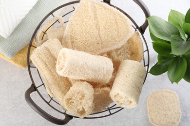 Photo of Different loofah sponges in basket and towels on light grey table, flat lay