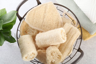 Photo of Different loofah sponges in basket and towels on light grey table, flat lay