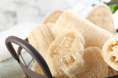 Photo of Different loofah sponges in basket on blurred background, closeup