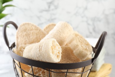 Photo of Different loofah sponges in basket and towels on table, closeup