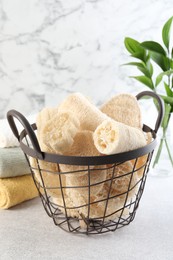 Photo of Different loofah sponges in basket and towels on light grey table