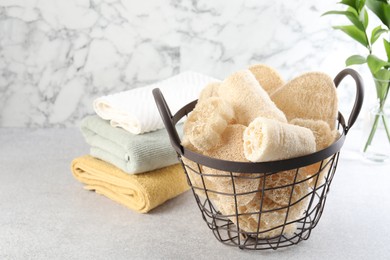 Photo of Different loofah sponges in basket and towels on light grey table