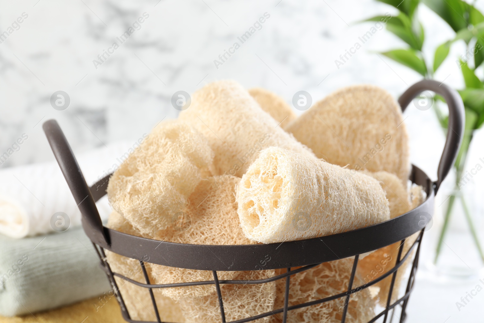 Different loofah sponges in basket and towels on table, closeup Photo of Different loofah sponges in basket and towels on table, closeup