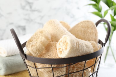 Photo of Different loofah sponges in basket and towels on table, closeup