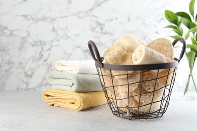 Photo of Different loofah sponges in basket and towels on light grey table